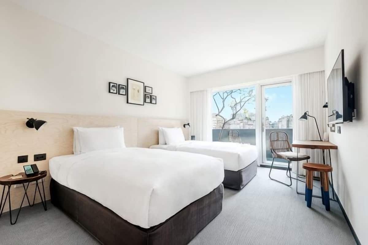 A hotel room with two beds, a desk, a chair, and a large window.