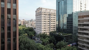 Un edificio alto con una facciata moderna in vetro, immerso nel verde e circondato da altri edifici.