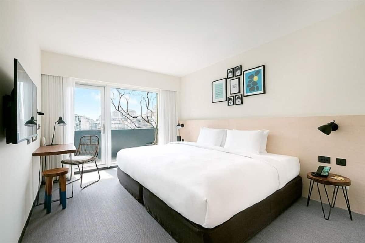 A hotel room with a large bed, a desk, a chair, and a small table with a phone.