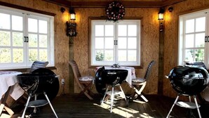 A room with two barbecue grills, a table with chairs, and large windows with curtains. - Spa Pension Basso (Sokcho)