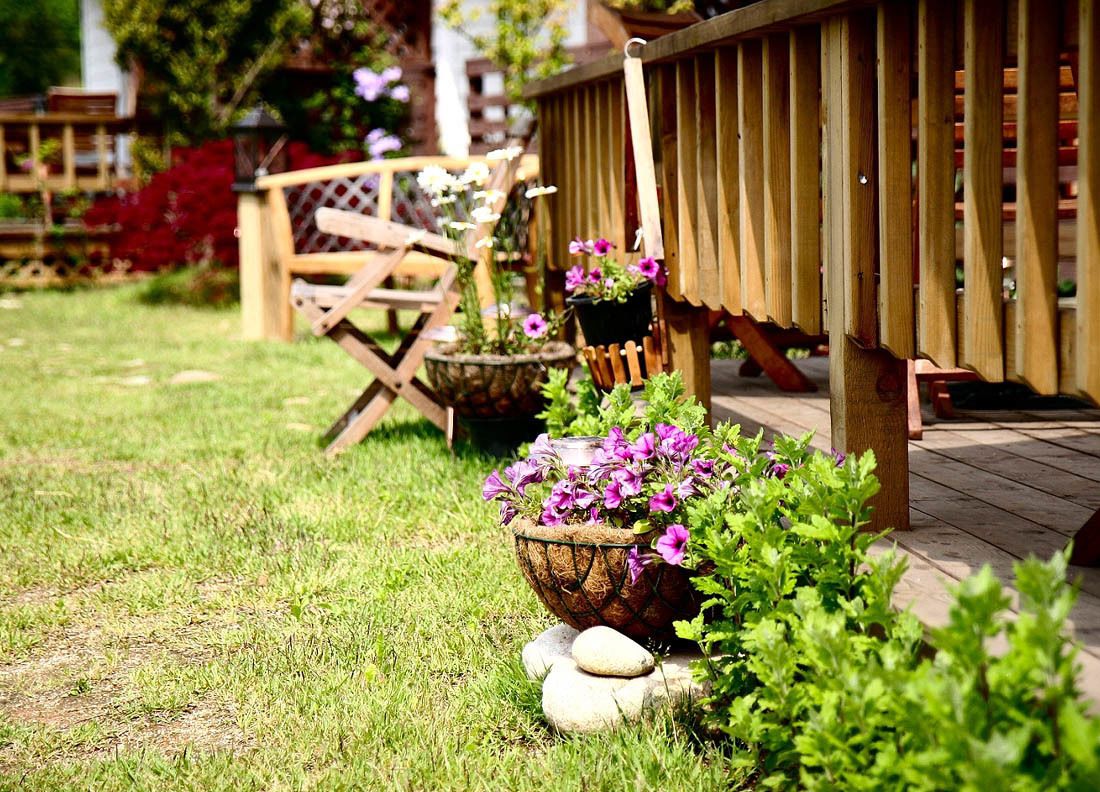 A wooden deck with a railing, surrounded by a garden with various potted plants and flowers.