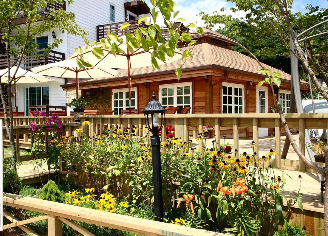 Une maison en bois dotée d’un balcon, entourée d’un jardin où poussent différentes sortes de fleurs et de plantes.