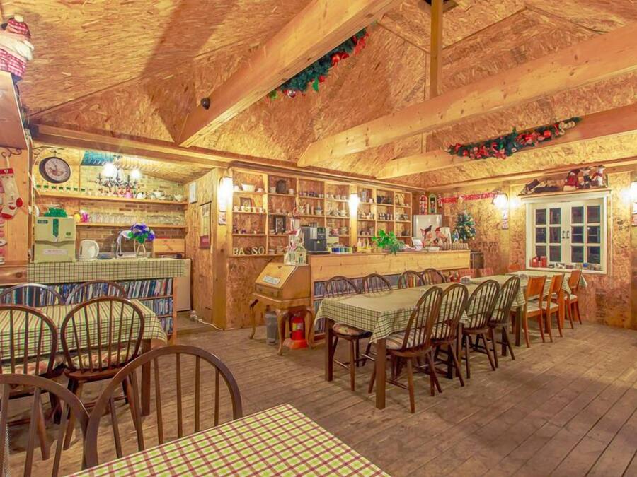Un café rústico y acogedor con interiores de madera, una barra y diferentes opciones de asientos, incluyendo mesas y sillas.