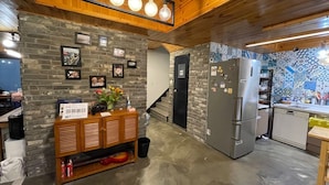 A kitchen with a brick wall, wooden cabinets, a refrigerator, and a tiled backsplash. - Twin Rabbit Guesthouse (Seoul)