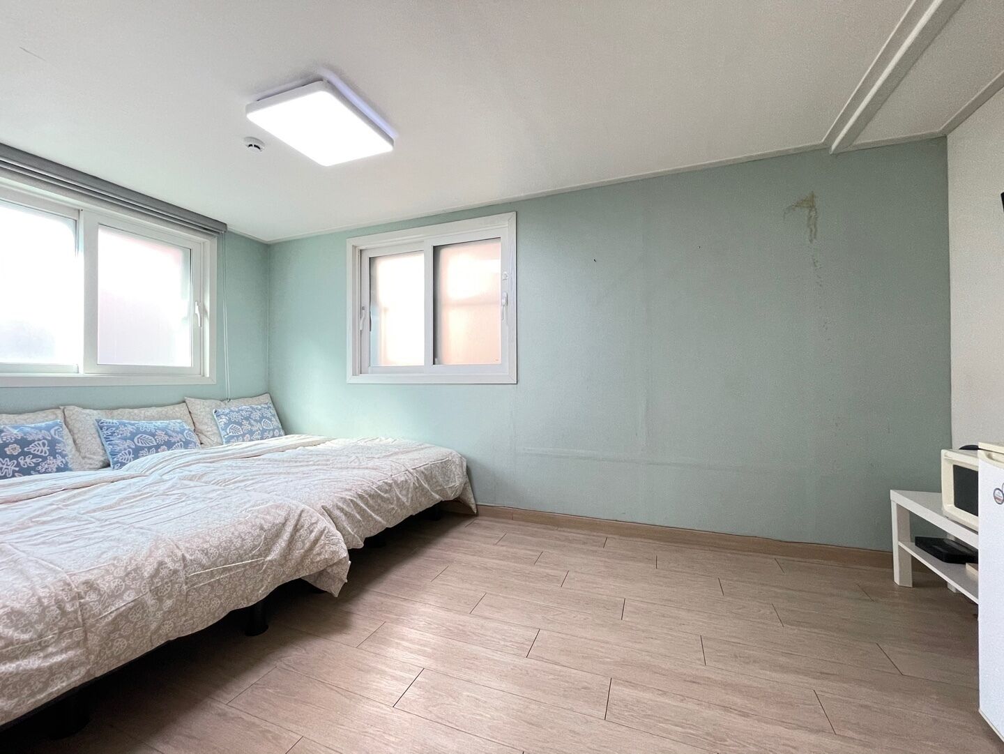 A bedroom with a bed, two windows, a ceiling light, and a white shelf.