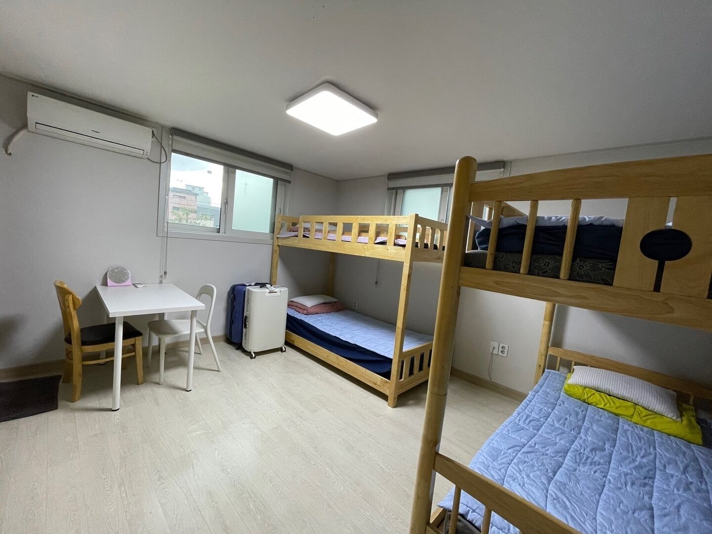 Ett studentrum med våningssängar, ett skrivbord, en stol och en resväska.