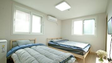 A bedroom with two beds, a window, a ceiling light, and a small table with a vase.