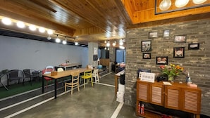A spacious indoor area with a long wooden table, several chairs, a brick wall with framed pictures, and a small wooden cabinet with a guitar. - Twin Rabbit Guesthouse (Seoul)