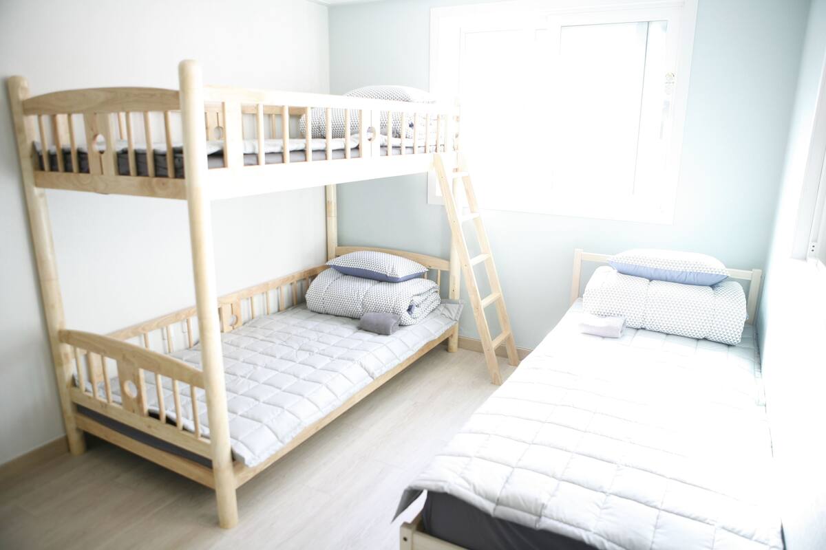 A bunk bed room with a ladder, a window, and a door.