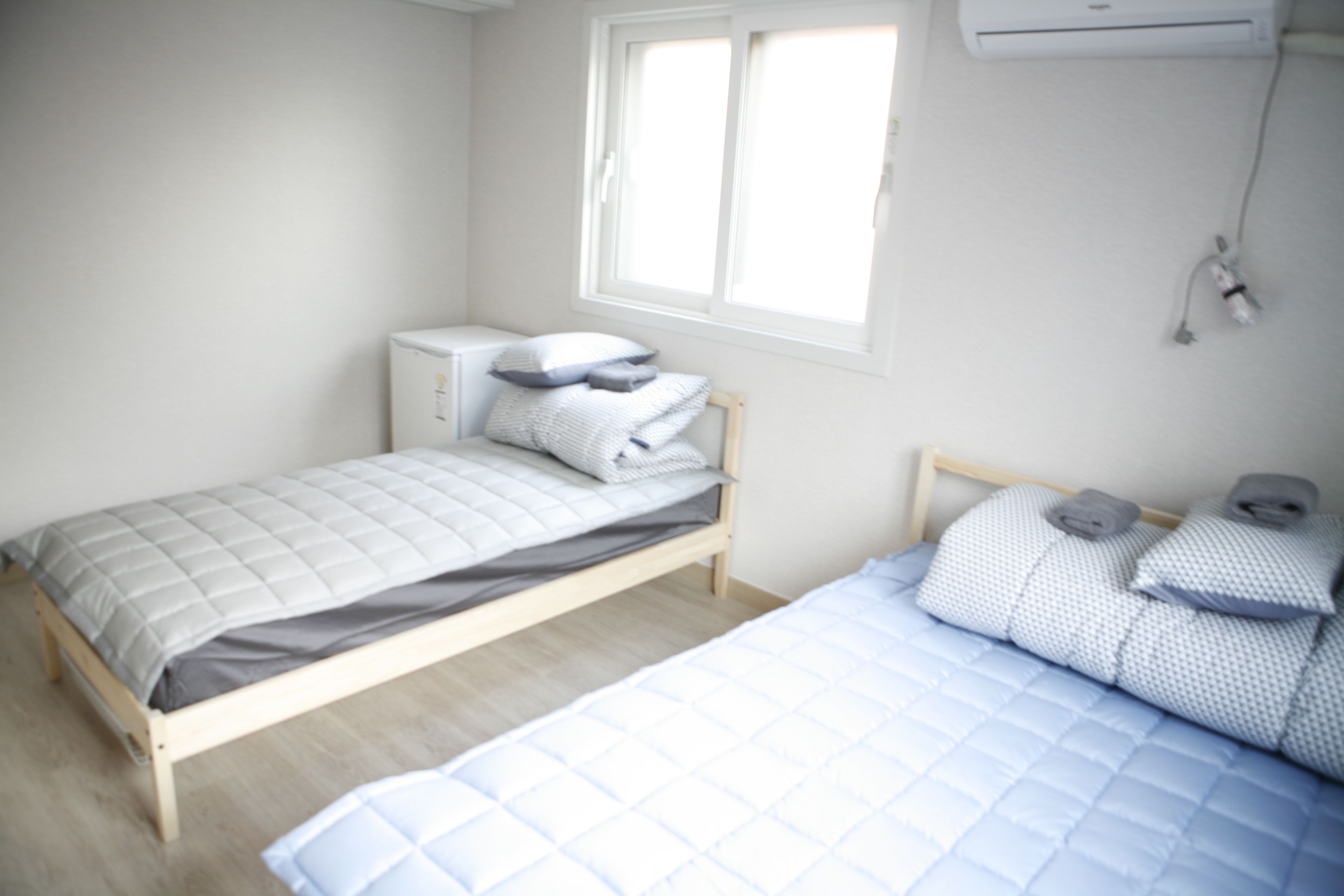 A bedroom with two beds, a window, and an air conditioning unit.