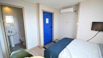A hotel room with a bed, a chair, a sink, and a toilet.