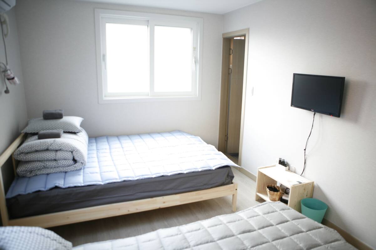 A bedroom with a single bed, a small desk, a television, and a window.