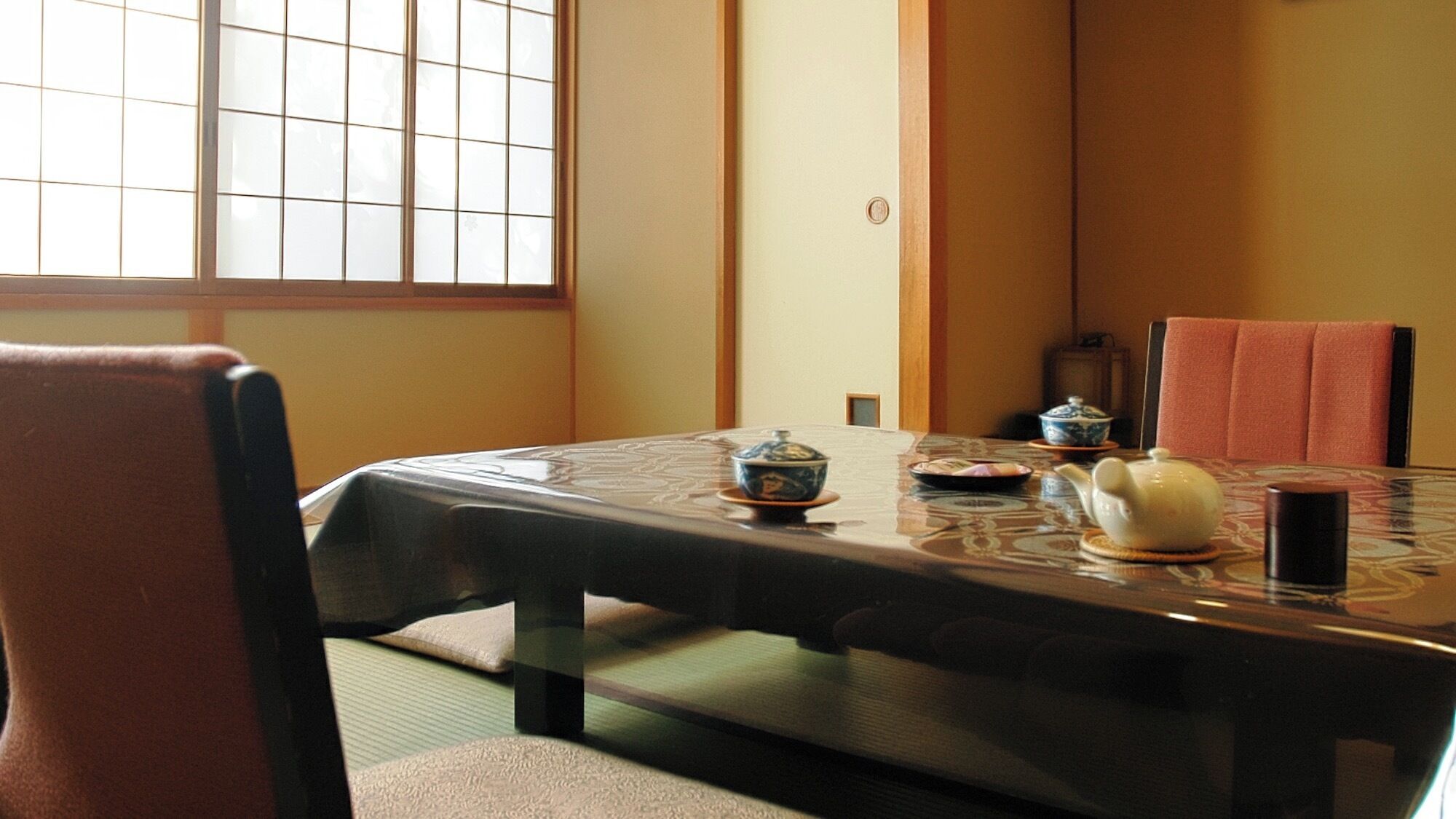 Une pièce de style japonais traditionnel, avec un sol recouvert de tatamis, une petite table basse accompagnée d’un service à thé et une porte coulissante à motifs géométriques.