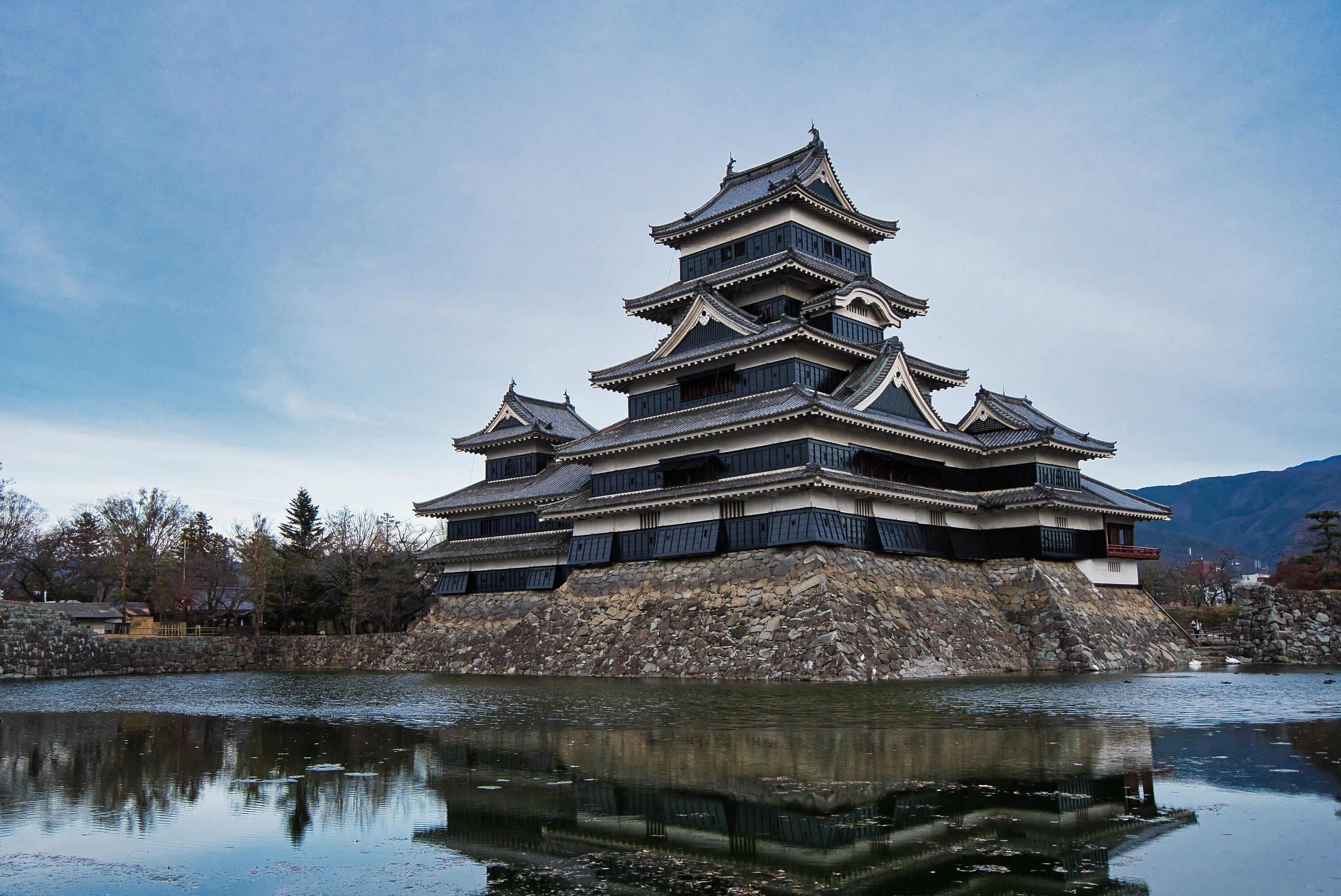 A traditional Japanese castle with multiple tiers, located beside a calm body of water.