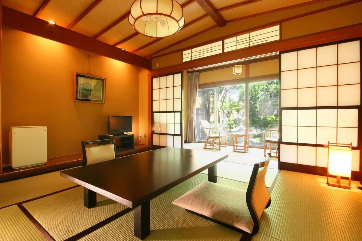 Een traditionele Japanse kamer met tatami vloerbedekking, een lage tafel, een televisie en schuifdeuren die leiden naar een buitenruimte.