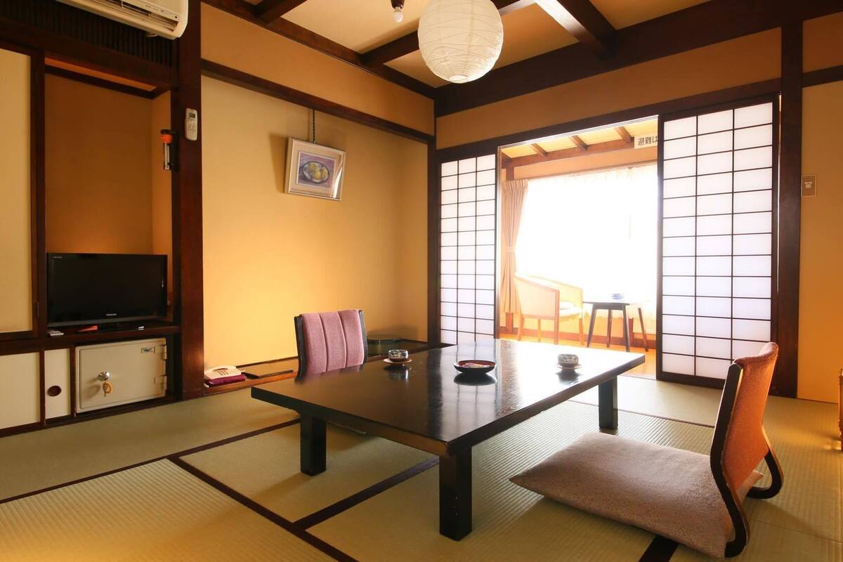Een traditionele Japanse kamer met tatami vloerbedekking, een lage tafel, een televisie en schuifdeuren.