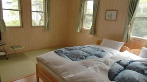 A bedroom with a wooden bed, green curtains, a small table, and a window. - Pension Souvenir (Iki)