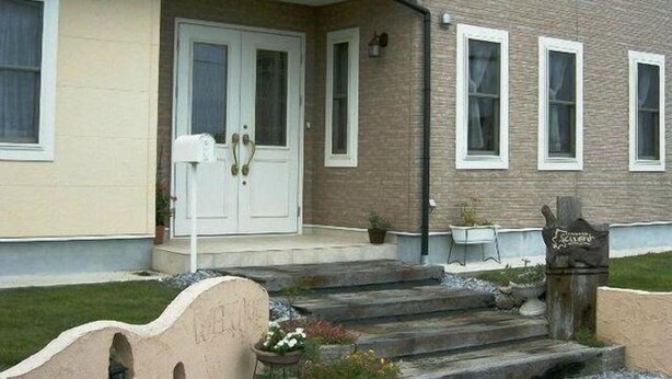 A two-story building with a front porch, a mailbox, and a small outdoor seating area. - Pension Souvenir (Iki)