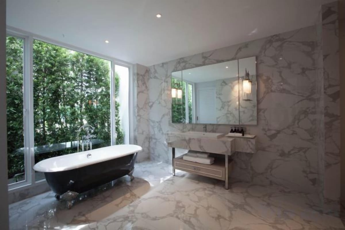 Une salle de bain moderne avec une baignoire sur pieds, un grand miroir et un sol en marbre.