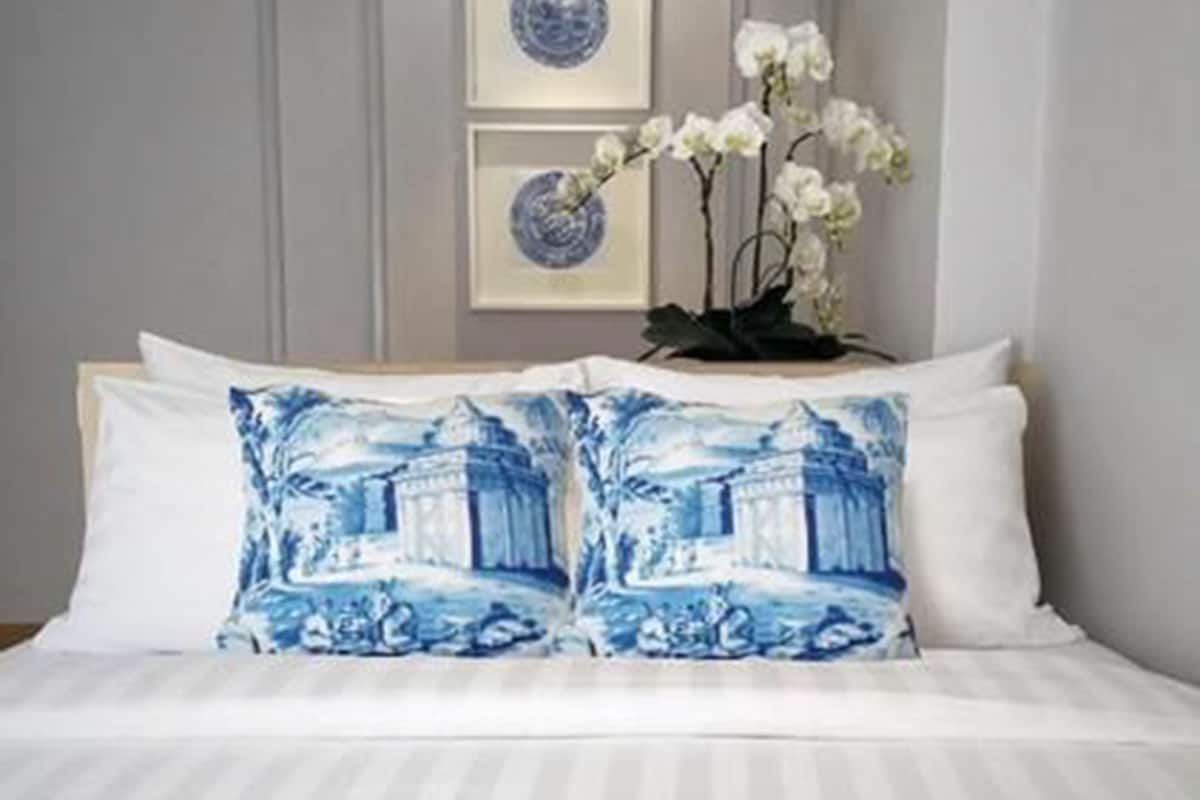 Un lit bien fait, avec une literie blanche et deux oreillers bleus représentant une scène aux couleurs bleu et blanc.
