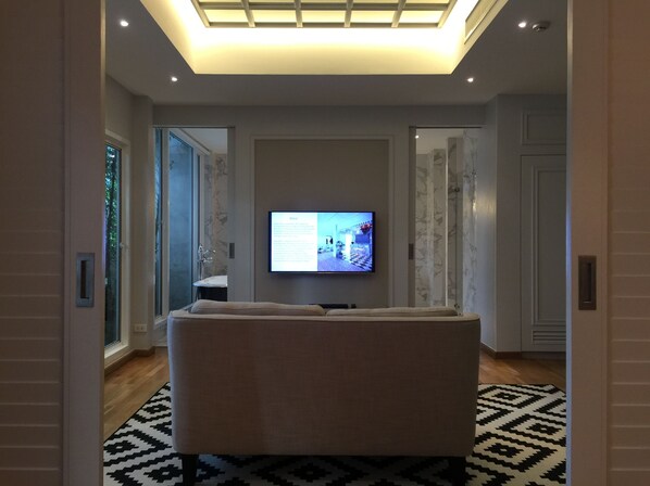Un salon moderne avec un téléviseur à écran plat fixé au mur, un canapé beige et un tapis à motifs.