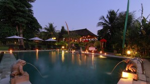 A swimming pool with a frog statue, surrounded by palm trees and a building with a thatched roof. - Subak Tabola Villa (Sidemen)