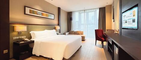 A hotel room with a bed, bedside table, lamp, TV, and a desk with a chair.