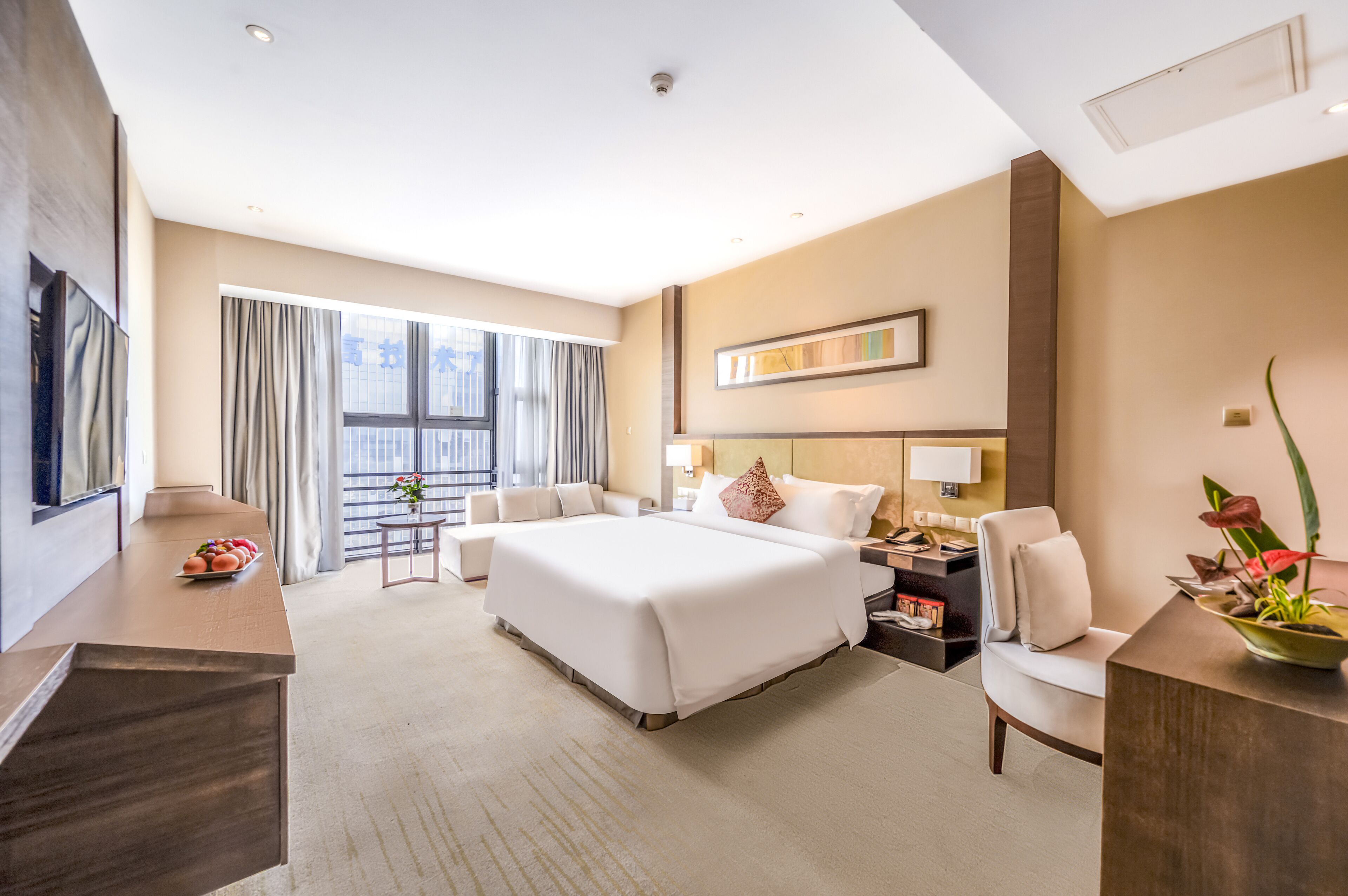 A modern hotel room with a large bed, a desk, a chair, a nightstand, and a view of the outdoors.