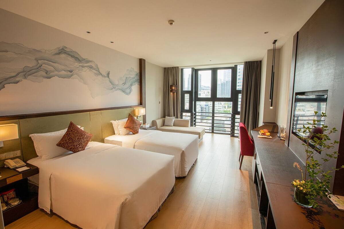 A hotel room with two beds, a desk, a chair, and a large window with a city view.
