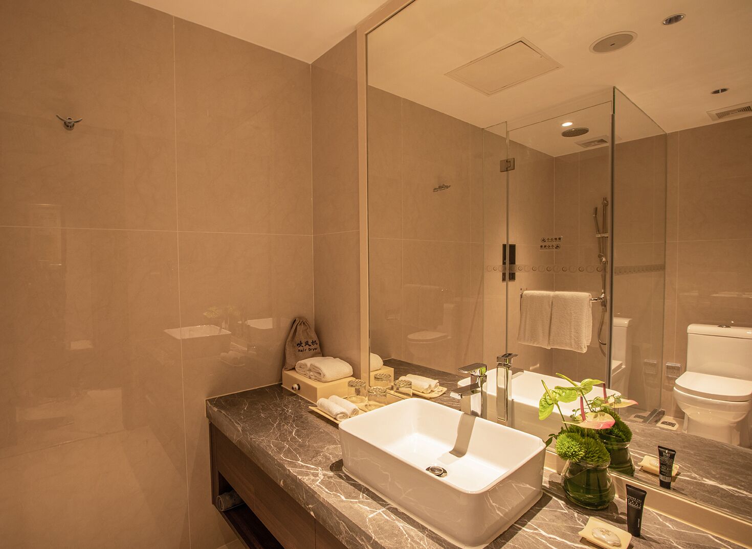 A modern bathroom with a large mirror, a marble countertop, a sink, a shower, and a toilet.