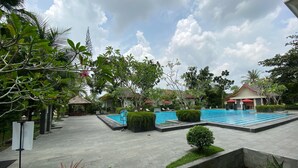 A swimming pool area with a tiled deck, surrounded by greenery and a small water feature. - Grand Zuri Hotel Duri (Mandau)