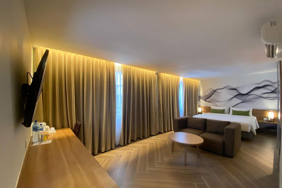 Ein modernes Hotelzimmer mit einem großen Bett, einer Couch, einem Couchtisch und einem an der Wand befestigten Fernseher.