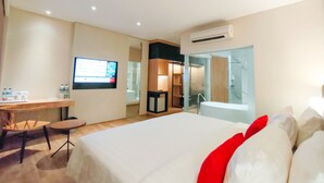 A hotel room with a bed, a desk, a TV, and a bathroom with a glass shower. - Grand Zuri Hotel Duri (Mandau)