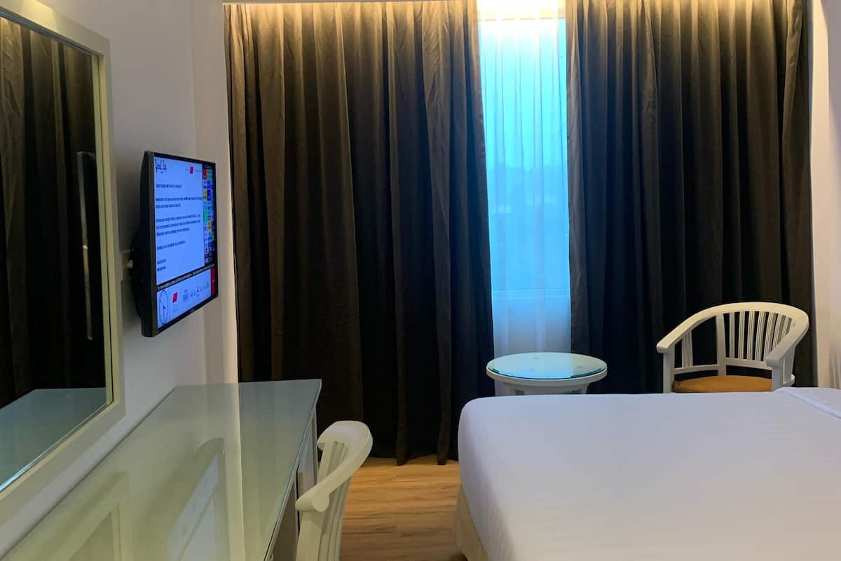 Ein Hotelzimmer mit einem Bett, einem Schreibtisch mit Stuhl, einem kleinen Tisch, einem Fernseher und einem Fenster mit Vorhängen.