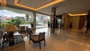 A modern lobby with glass walls, a reception desk, wicker furniture, and a clean, polished floor. - Grand Zuri Hotel Duri (Mandau)