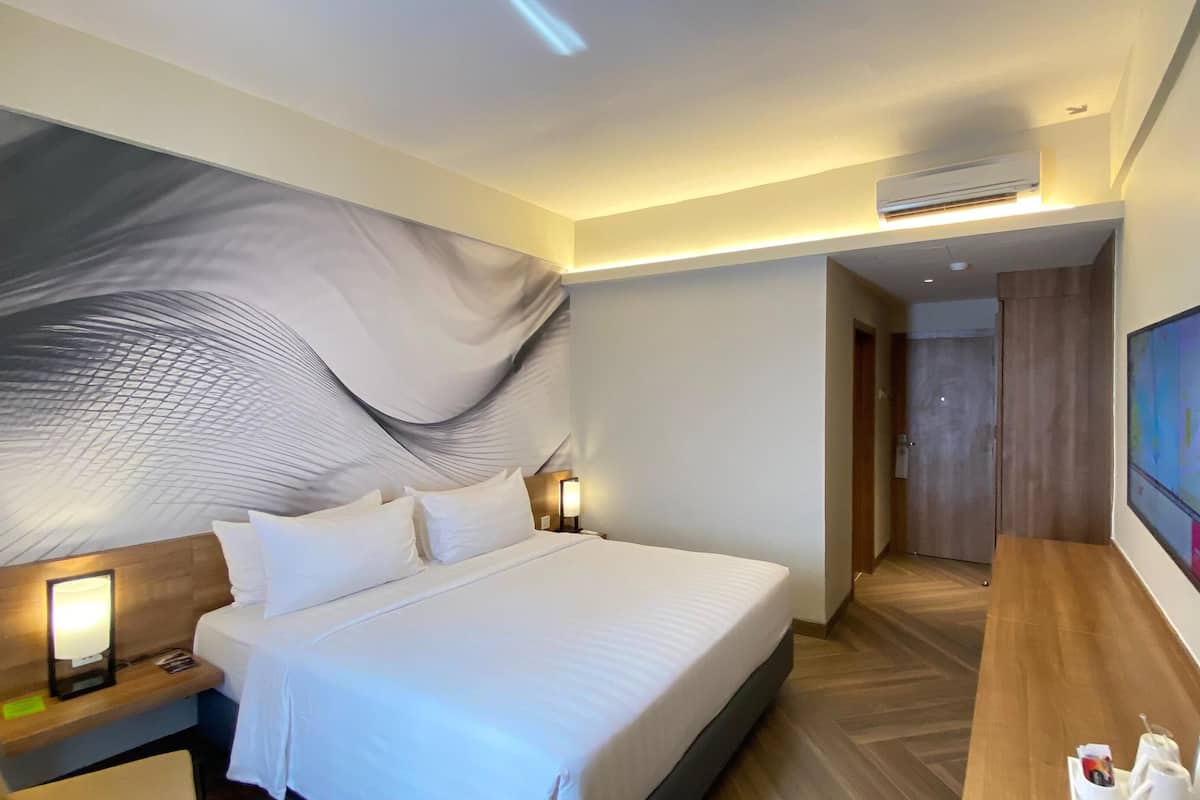 Ein Hotelzimmer mit einem großen Bett, Nachttischlampen, einem Flachbildfernseher und einer Klimaanlage.