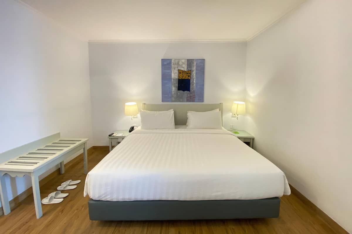 Ein ordentlich eingerichtetes Hotelzimmer mit einem großen Bett, zwei Nachttischen mit Lampen, einer Bank und einem an der Wand befestigten Kunstwerk.