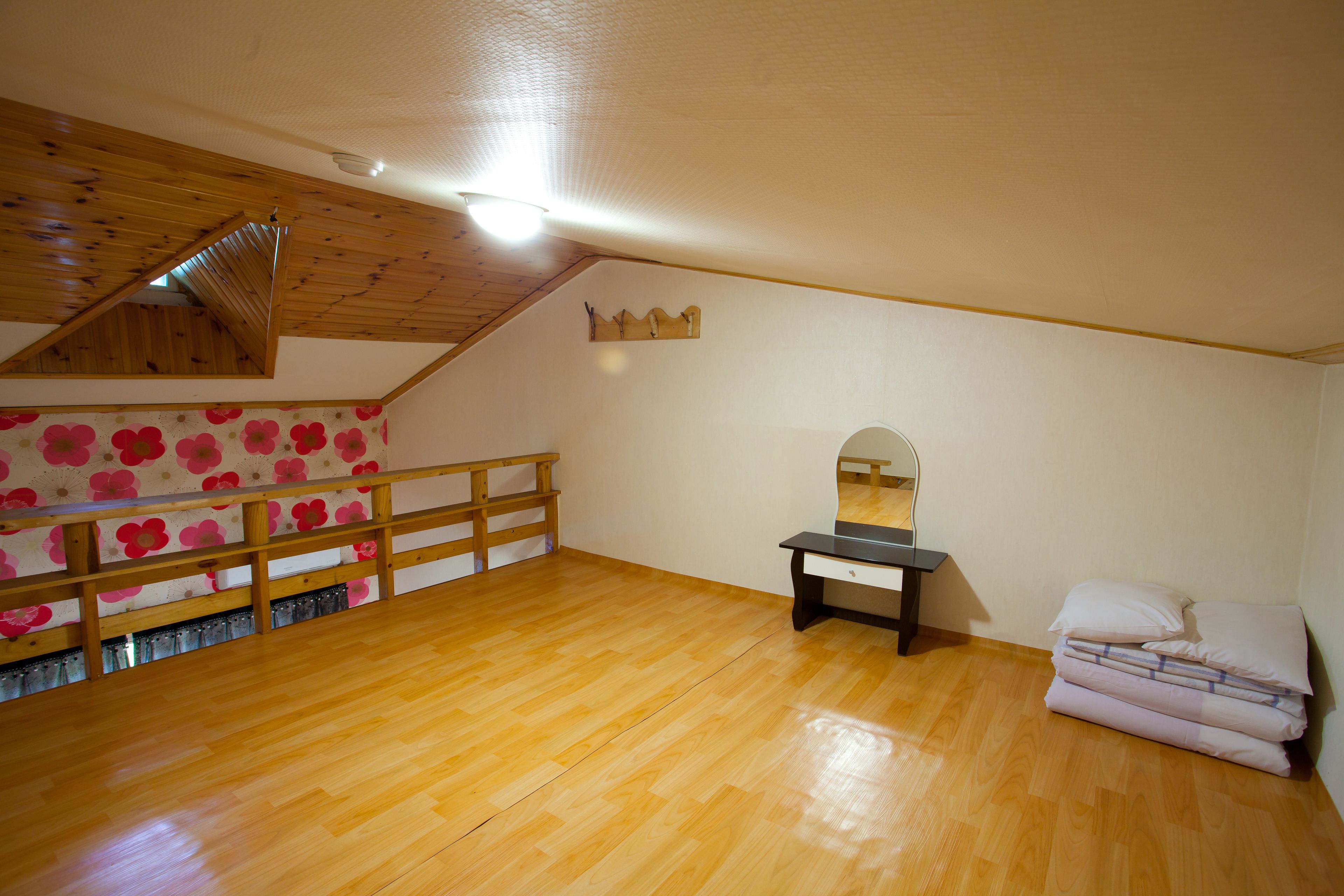 Une pièce avec un plancher en bois, un escalier en bois, un lit, une commode et un miroir.