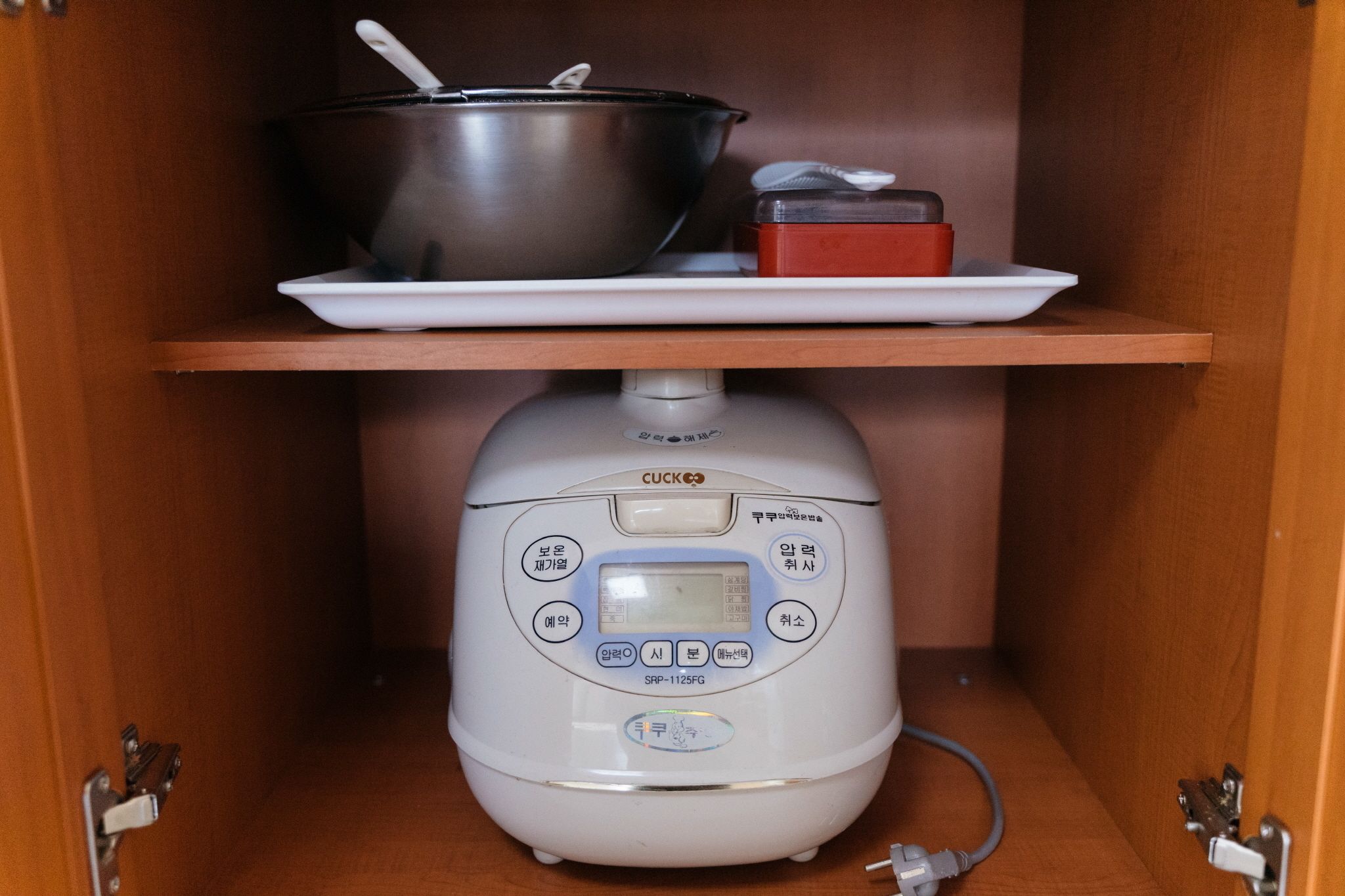 A kitchen with a rice cooker on the counter, a pot on a shelf, and a small red container.