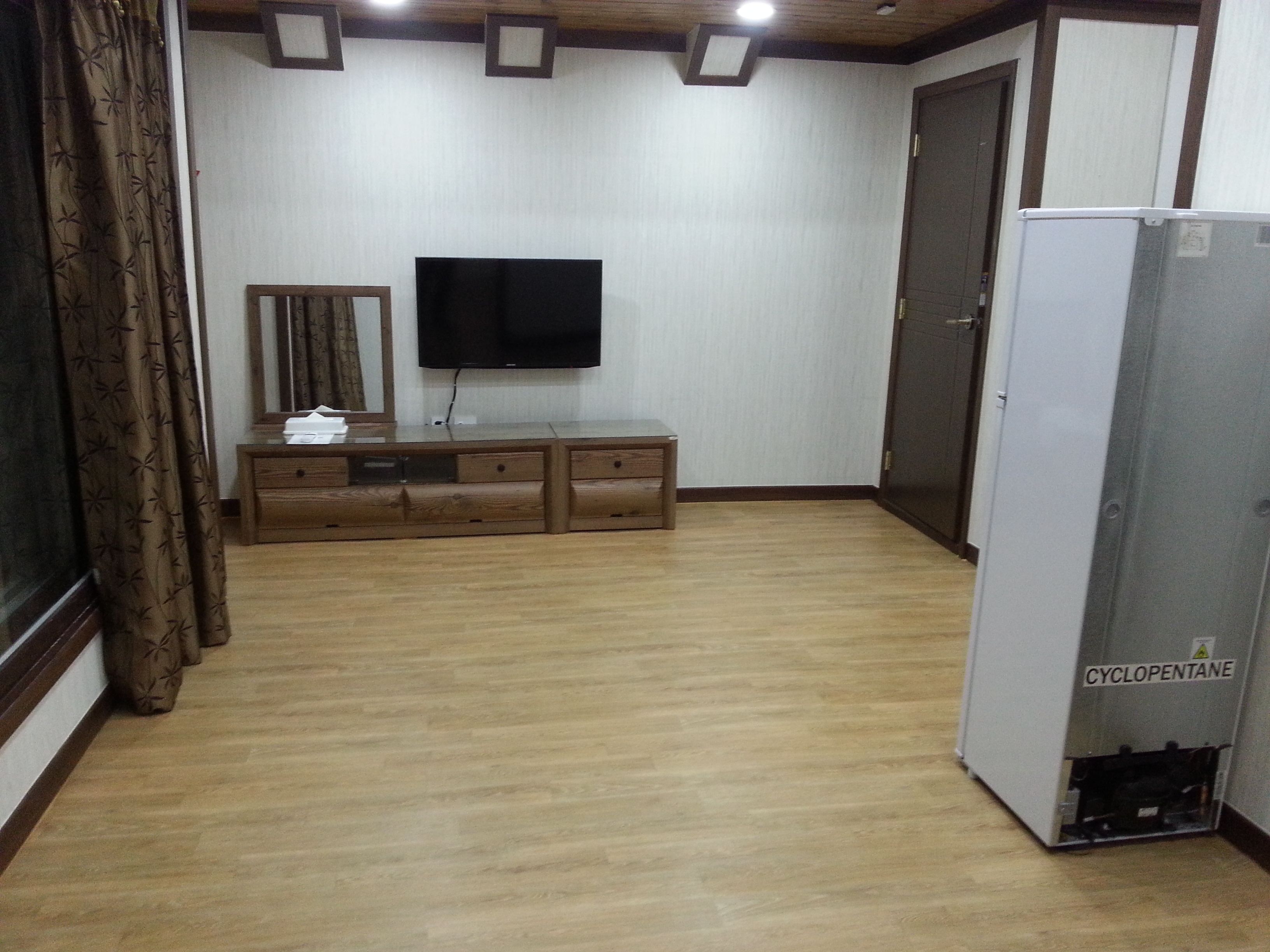 A room with a wooden cabinet, a flat-screen TV mounted on the wall, and a white refrigerator.