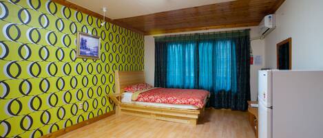 A room with a bed, a wooden floor, a wall with circular patterns, a window with curtains, and a refrigerator.