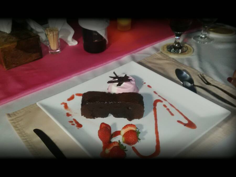 Un plato de postre con pastel de chocolate, fresas y una cucharada de crema sobre un plato blanco.