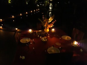 A dimly lit dining area with candles, a vase with flowers, and a table set for two. - Pandawa Village (Sukasada)