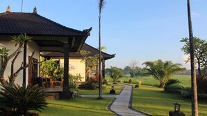 Un edificio de estilo tradicional con tejado de tejas, rodeado por un jardín cuidado con palmeras y un camino pavimentado que lleva a la entrada.
