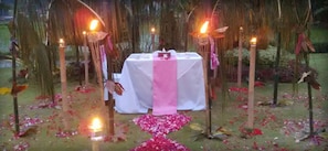 An outdoor wedding setup with a white table, pink drapery, and candles.
