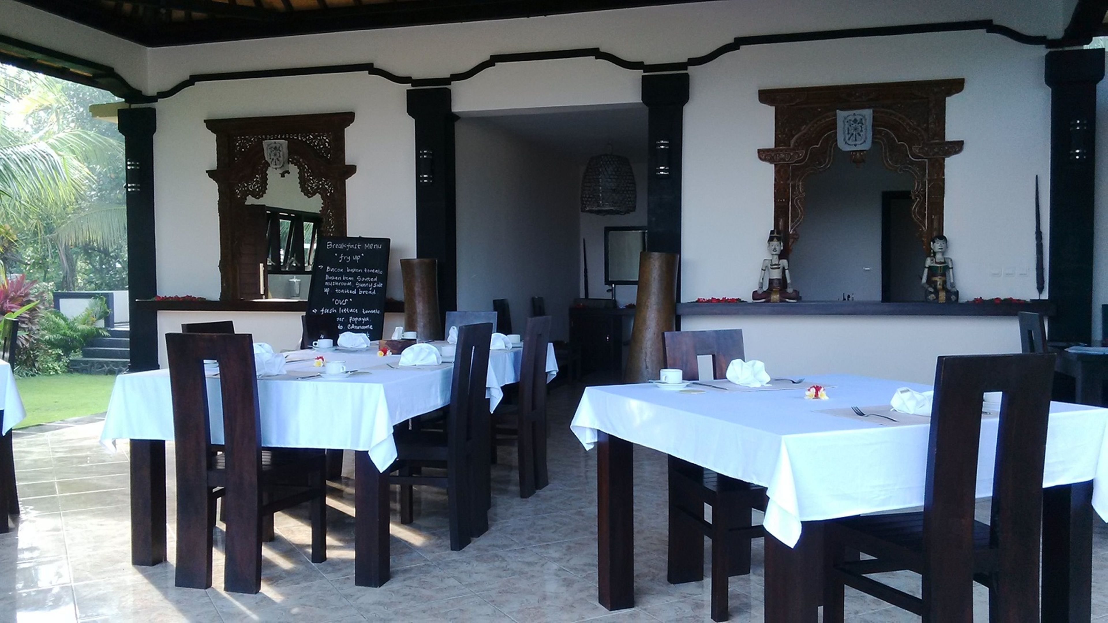 Un área de comedor al aire libre con mesas y sillas, un menú en una pizarra y elementos decorativos.