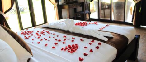 A hotel room with a bed adorned with rose petals and a folded white towel.