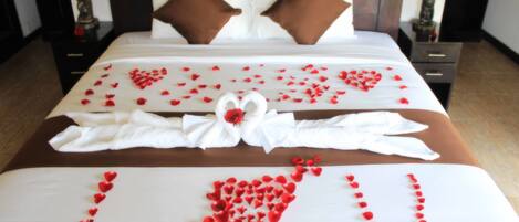 Una cama impecable con pétalos de rosa dispuestos en forma de corazón que deletrea “Te amo” y una toalla blanca con un lazo.