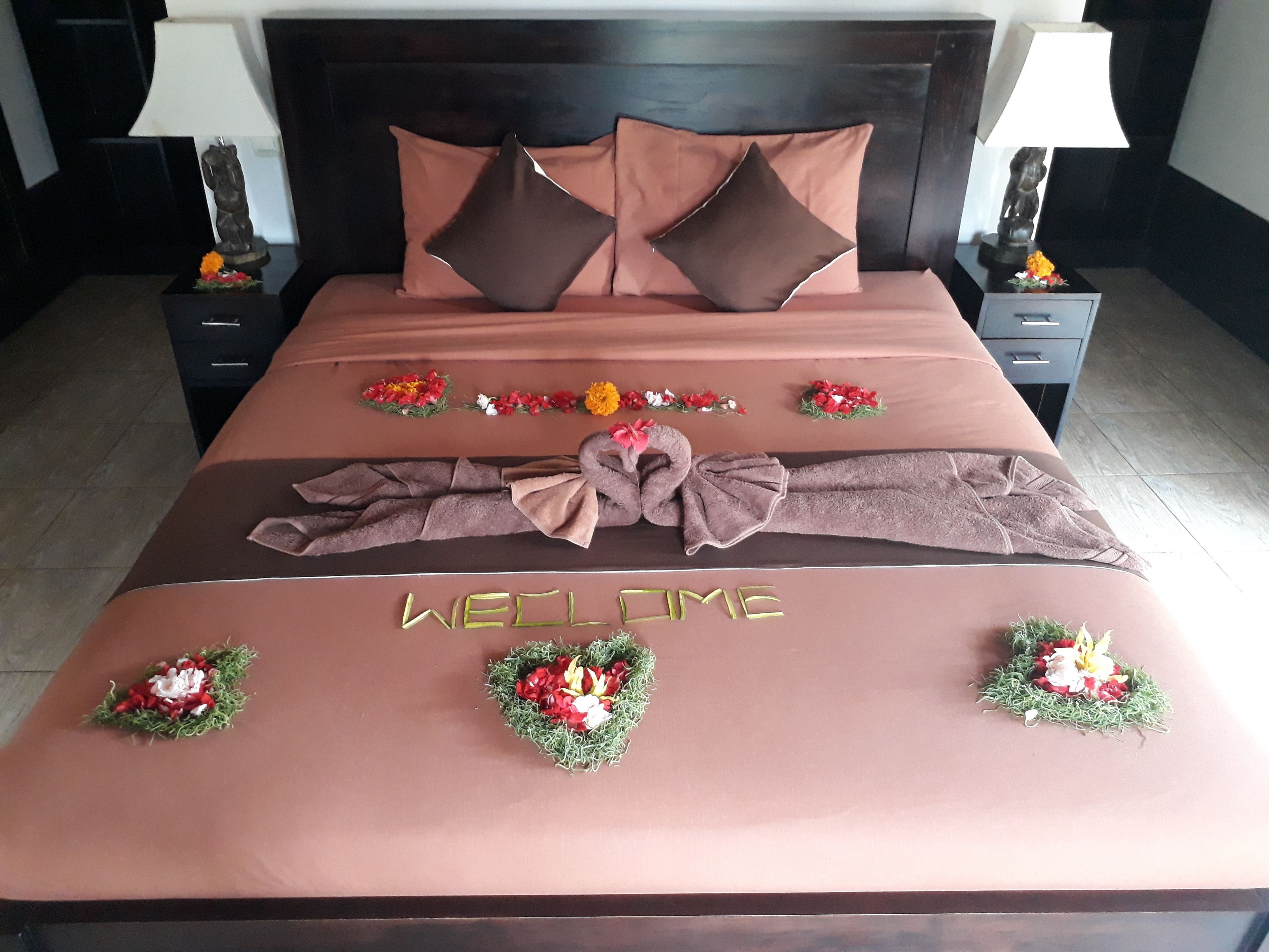 Una cama bien hecha con un cartel que dice 'WELCOME', almohadas decorativas y arreglos florales.