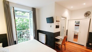 Une chambre d’hôtel équipée d’un lit, d’un bureau, d’une chaise, d’une télévision, d’une armoire et d’une fenêtre avec des rideaux.